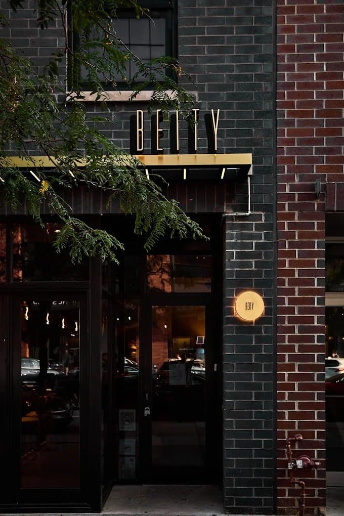 Beity’s entrance on Fulton Street at dusk: gold BEITY lettering over the door, a lit round sign on dark brick, and a tree branch across the front